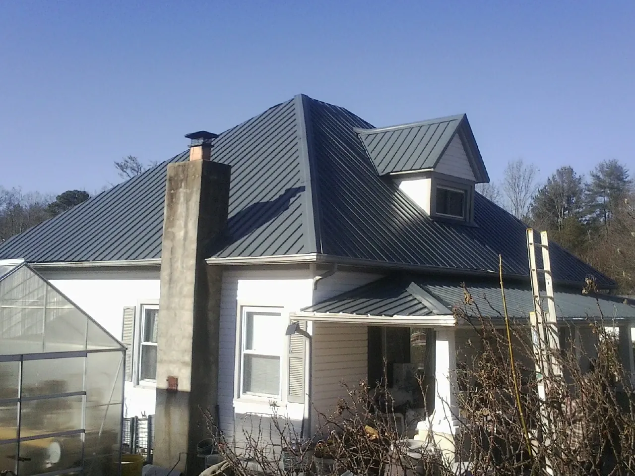 Dark blue standing seam metal roof on a white farmhouse with dormer — Slate & Tile Roof Repair by Roofing Brothers in Swartz Creek