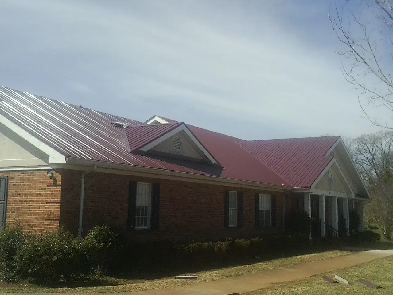 Red metal roof with gabled entries on a long brick building, from a Hail Damage Roof Repair job in Swartz Creek
