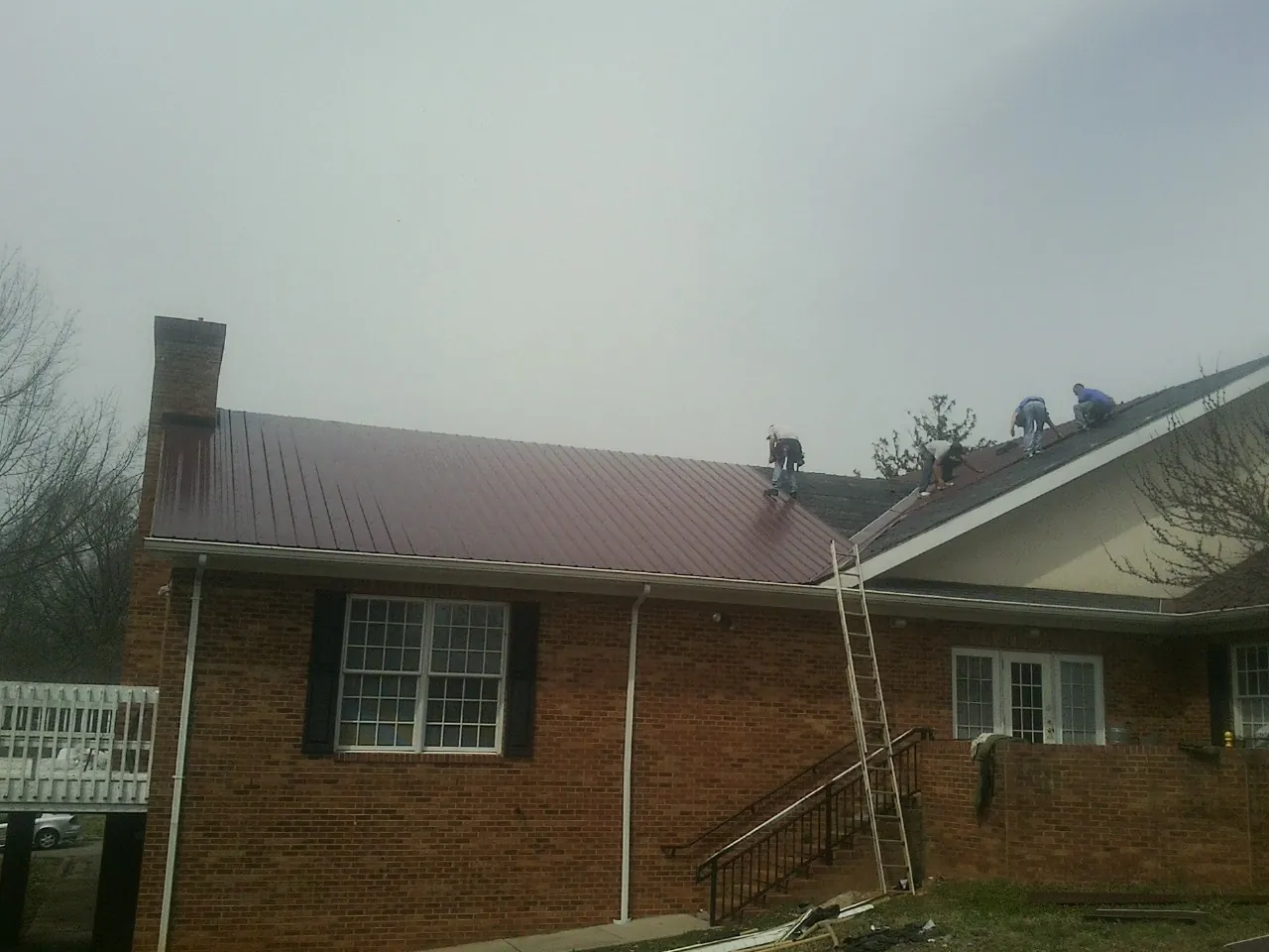 Crew setting red metal roofing panels on a brick home in Swartz Creek