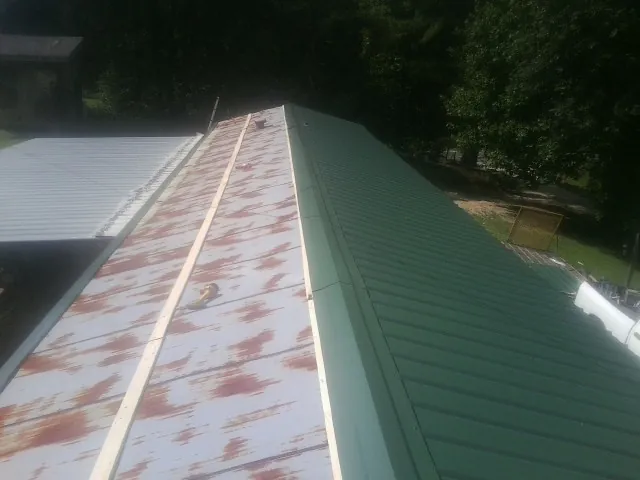 Old rusted panels beside newly installed green metal roofing — Wind Damage Roof Repair by Roofing Brothers in Swartz Creek