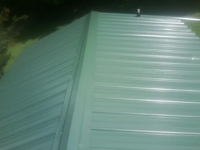 New green metal panels meeting at the ridge of a roof — Flat Roof Repair work by our crew in Swartz Creek