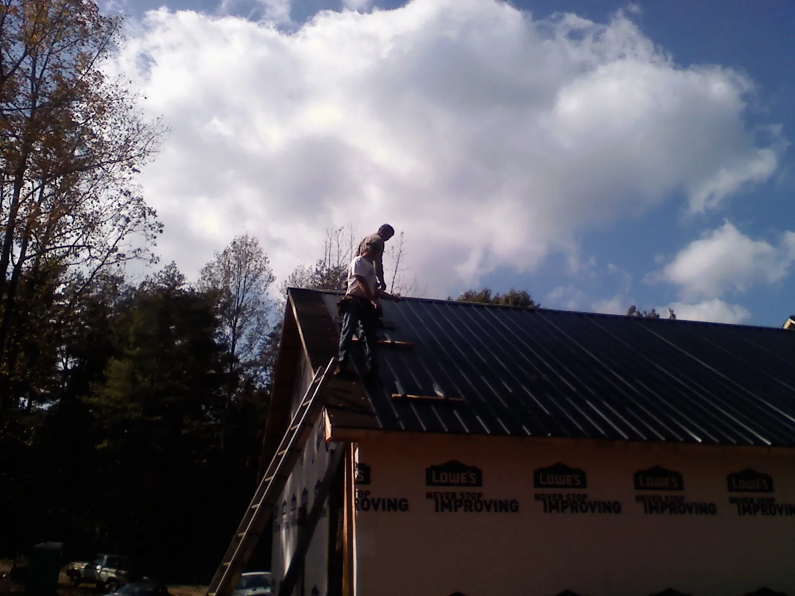 Roofer fastening dark metal panels high against a cloudy sky, from a Roof Inspection job in Swartz Creek