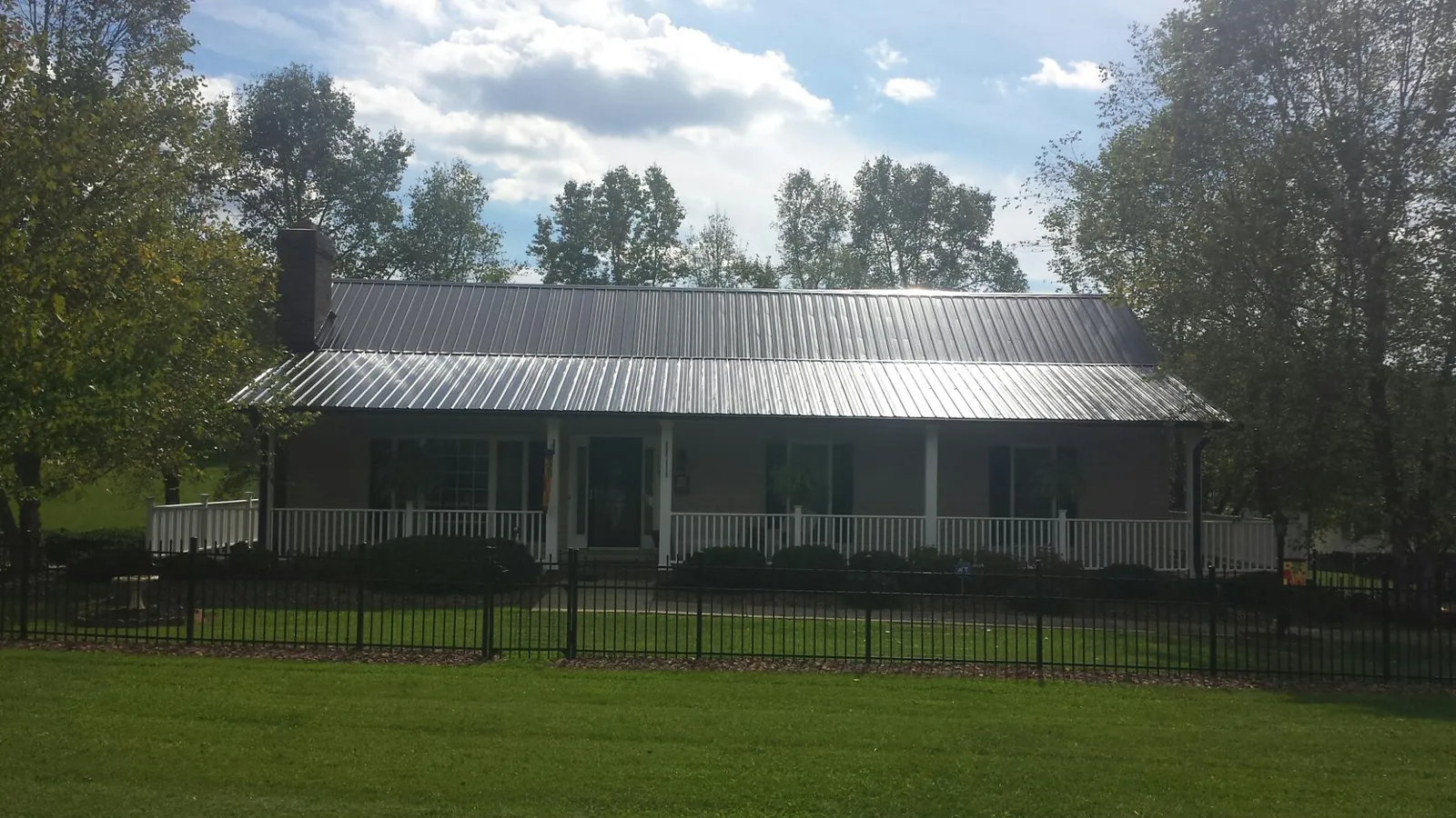 Gray metal roof on a brick ranch with a full width front porch — Gutter Guard Installation work by our crew in Swartz Creek