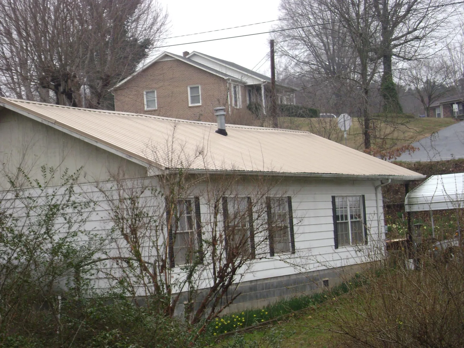 Tan metal roof on a white sided house set into a hillside — Commercial Roofing by Roofing Brothers in Swartz Creek