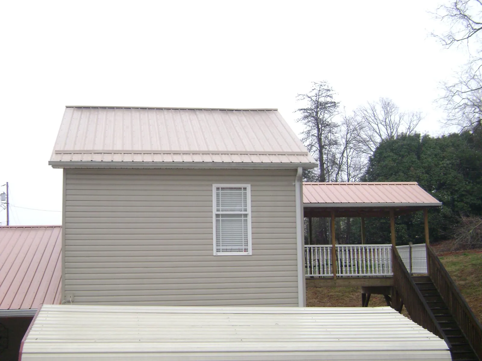 Tan metal roofs on a two story addition and attached porch, from a Roof Replacement job in Swartz Creek