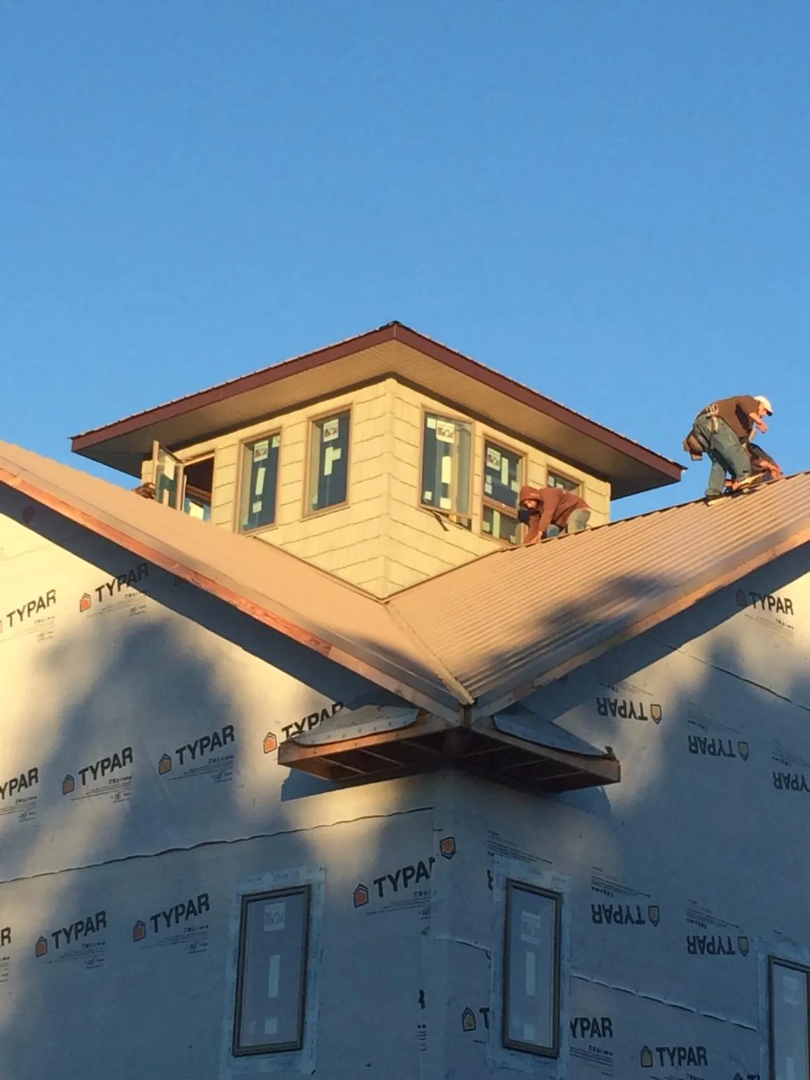 Roofers working around a rooftop cupola on a new metal roof at sunset — Roof Waterproofing in Swartz Creek by Roofing Brothers